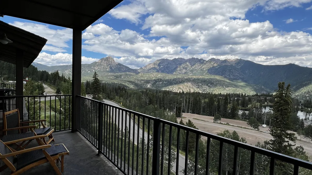 A private balcony outfitted with comfortable seating, overlooking a pristine mountain range, a tranquil lake, and lush trees. The scene is peaceful and inviting, encouraging guests to step outside, enjoy the fresh air, and immerse themselves in the natural beauty.