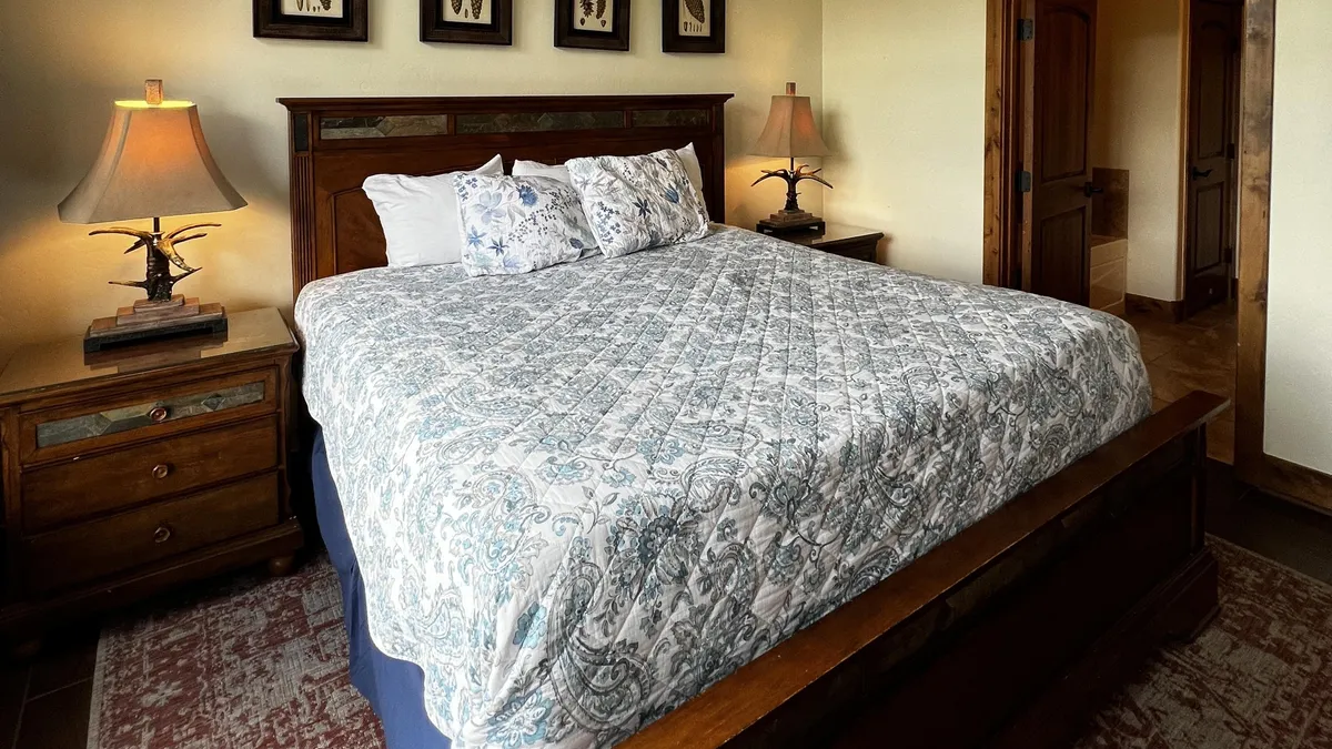 A king-sized bed with decorative pillows is flanked by nightstands and soft-lit lamps, while framed artwork above the bed sets a tranquil, cozy room atmosphere. The plush bedding and thoughtful decor invite relaxation and restful sleep.
