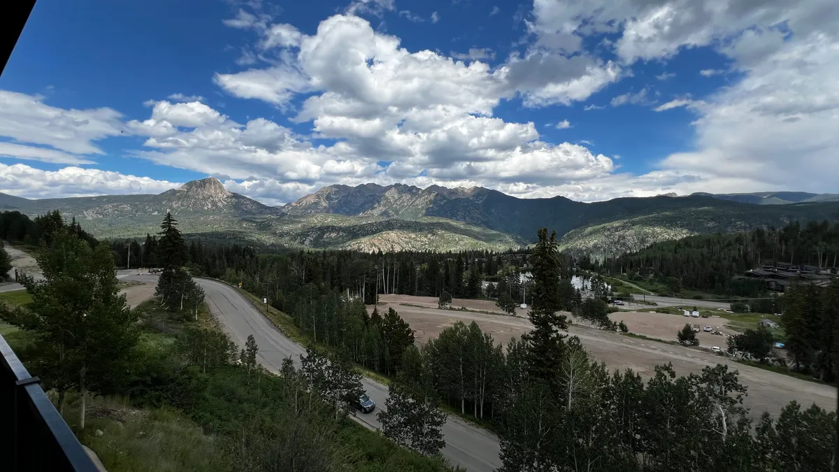 A breathtaking panorama of a mountain range with lush forests and winding roads below. The early morning sunrise casts a golden glow over the peaks and valleys, creating a serene and inviting atmosphere. Wisps of clouds float above, hinting at endless opportunities for outdoor adventure and exploration.