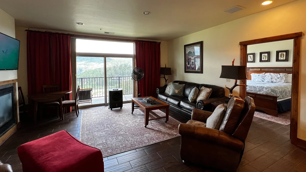 A cozy, open living and dining area featuring a large window that frames a striking mountain view. A comfortable sofa faces the window, with a dining table and a fireplace completing the inviting setting. The space encourages both relaxation and social gatherings, with the mountains ever-present through the glass.