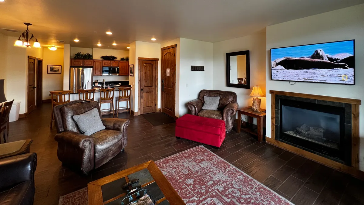 A spacious, stylish living area with comfortable leather sofas, a red accent chair, a glowing fireplace, and a view into the dining area. The scene is warm and welcoming, suggesting private condo comfort as described in the section.