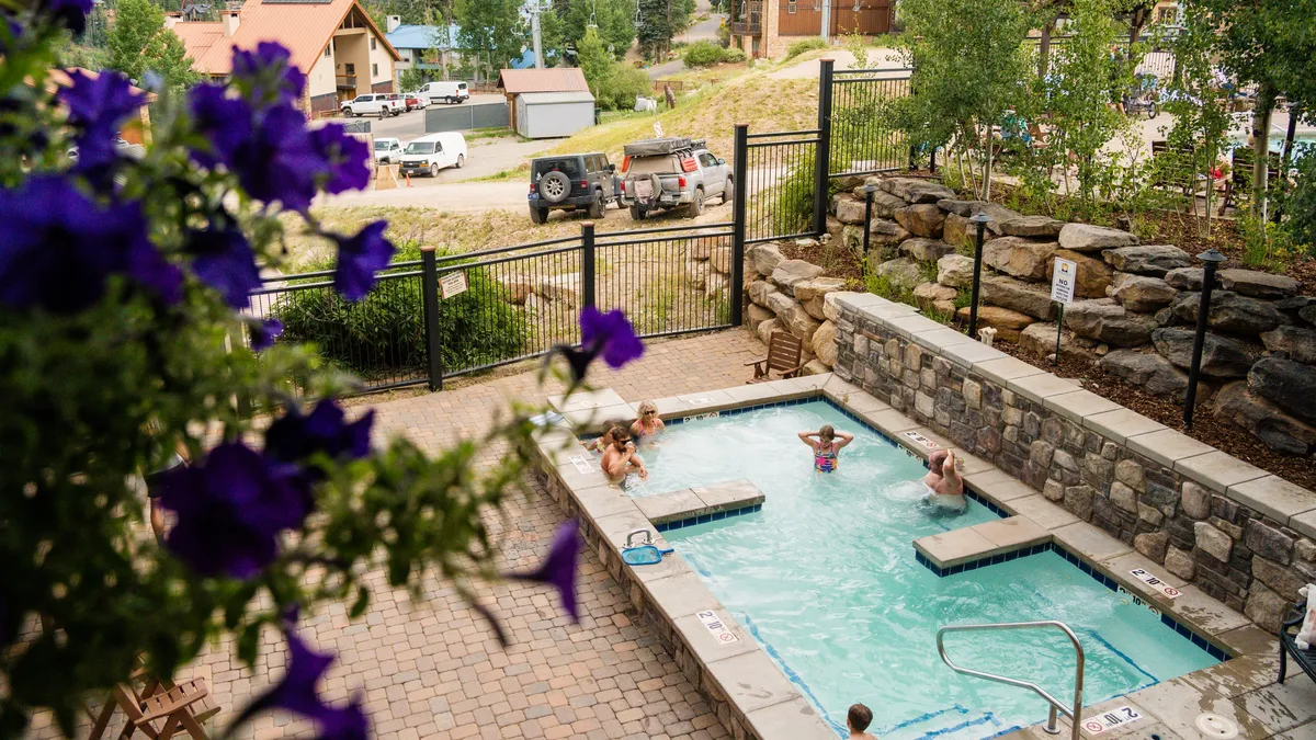 A bright exterior shot showcasing a hot tub and pool area surrounded by lush greenery. The scene suggests opportunities for swimming, lounging, and socializing in a relaxing mountain resort environment. The outdoor setting is inviting and makes clear the connection between leisure amenities and the natural surroundings.