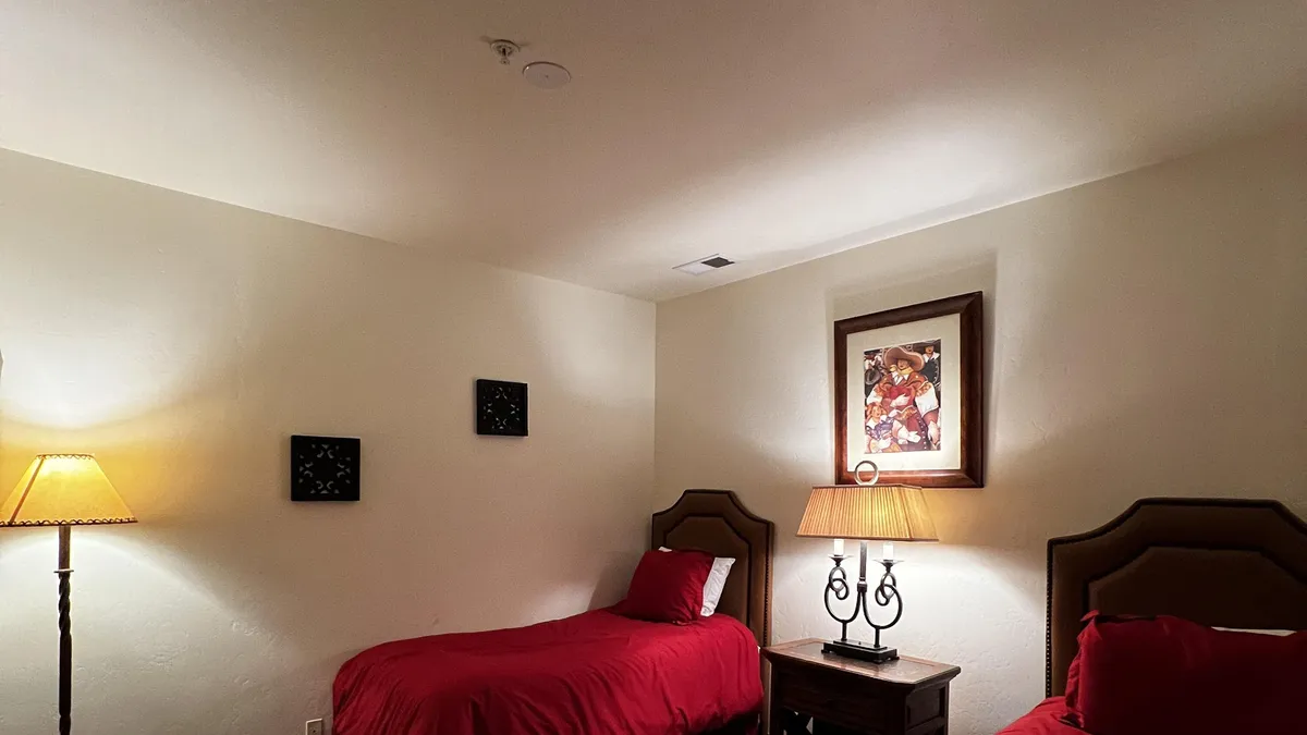 Two twin beds with bold red bedcovers are arranged with a shared bedside table and lamp, complemented by framed artwork on the wall, creating a warm, inviting space suited for children or guests.
