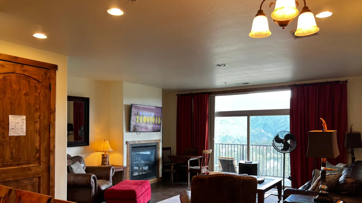 A warm, inviting living room with plush seating arranged around a fireplace. Large windows dominate one wall, offering a stunning, unobstructed view of the Needles Mountains. Red curtains add a touch of color, and the comfortable seating invites relaxation while enjoying the view or gathering with others.